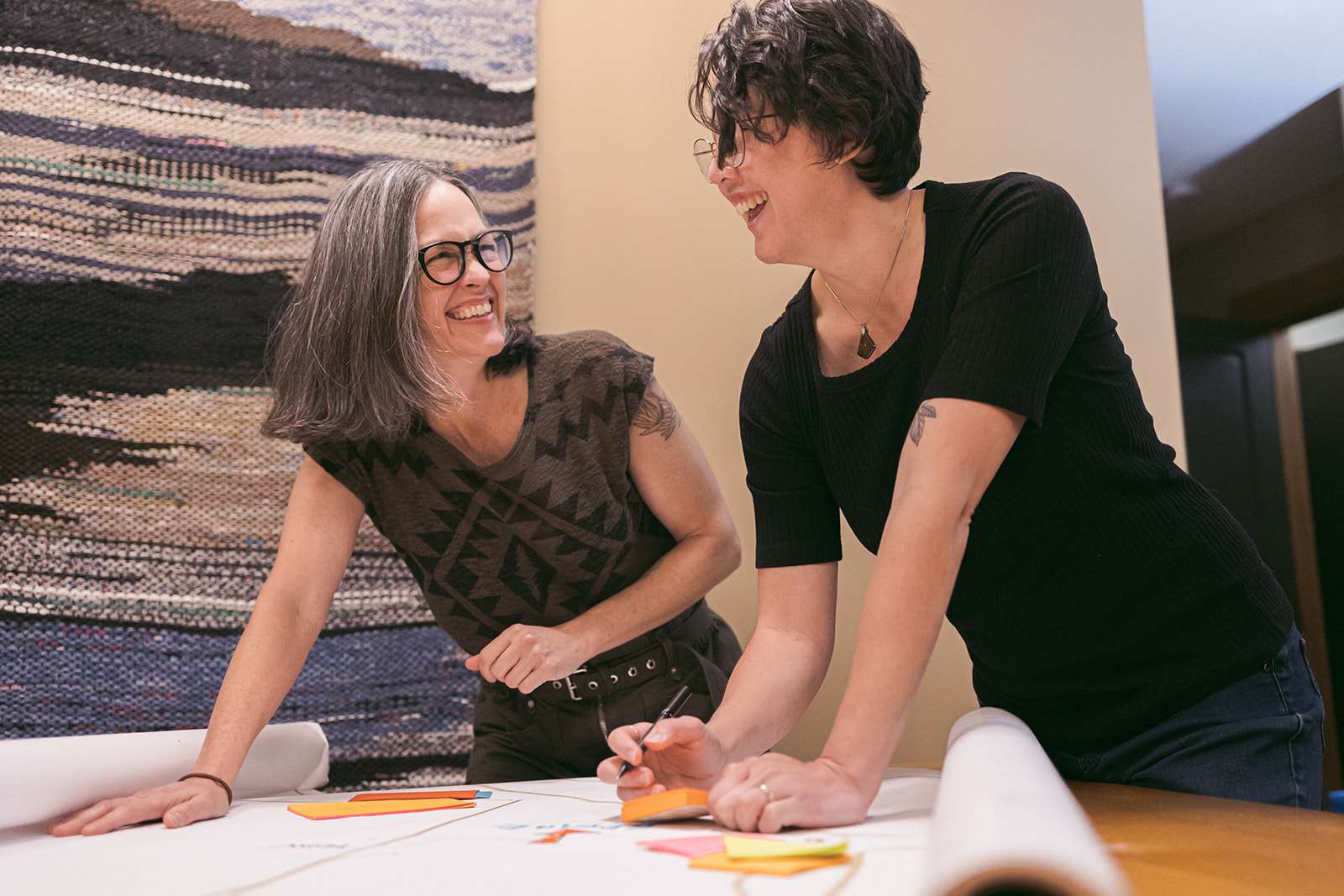 Two people laughing at work and writing on sticky notes.